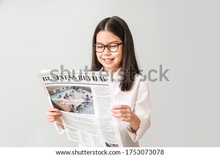 Cute little businesswoman with newspaper on grey background