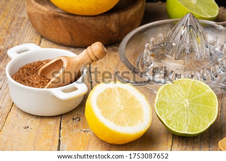 Close-up of half lemon, lime, brown sugar, juicer and wooden bowl with lemons, black background, horizontal