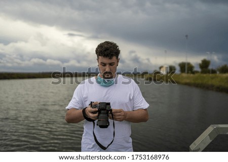 A male photographer with a facemask surrounded by the sea under a cloudy sky - COVID-19