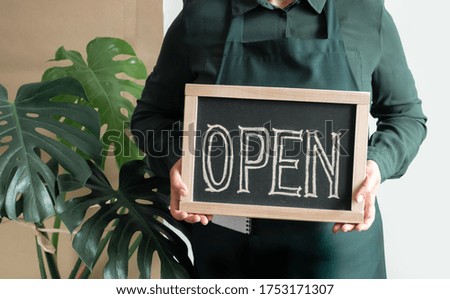 Woman's Hands Holds Dashboard with Text Open. Worker in apron Shows Opening of the Cafe or Market.
