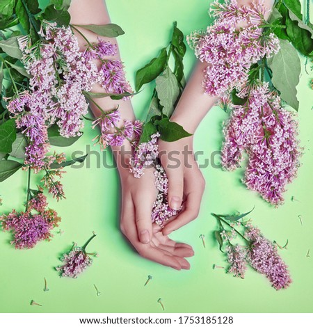Fashion art hands natural cosmetics women, bright purple lilac flowers in hand with bright contrast makeup, hand care. Creative beauty photo of a girl sitting at table on contrasting green background
