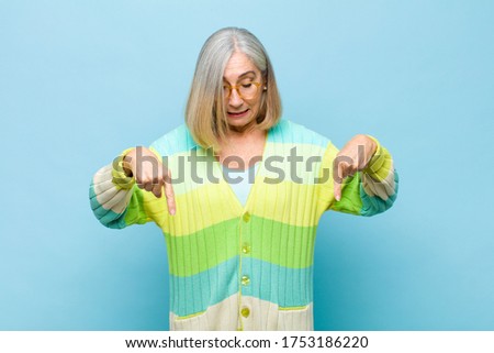 senior or middle age pretty woman with open mouth pointing downwards with both hands, looking shocked, amazed and surprised
