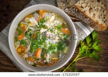 Chicken rice soup with vegetables in bowl and bread from above