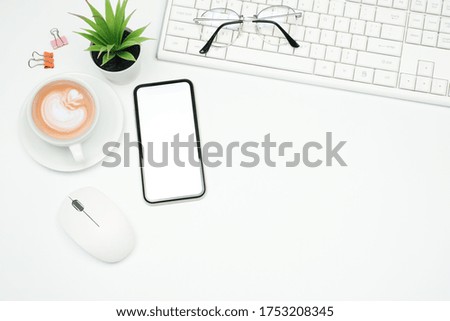 Flat lay, Workspace business office concept on white table desk with blank screen phone and mouse, Keyboard and green plant, coffee cup and paper clip, Top view  with copy space