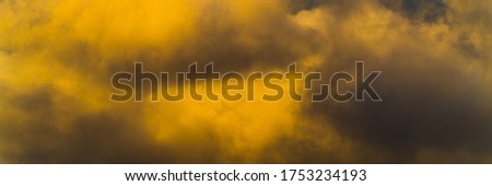 Panorama fluffy thunderstorm clouds illuminated by disappearing rays at sunset, thunderclouds floating across sunny blue sky to change season weather. Soft focus, motion blur sky landscape.