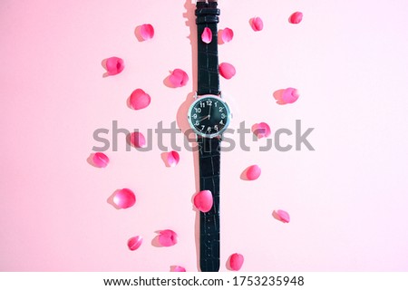 Black clock on a pink background with red rose petals. Valentin s Day.