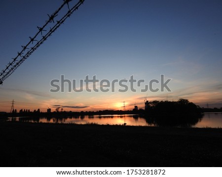 Urban city sunset sky above Walthamstow wetlands with silhouette fence and barbed wire reflecting in the water