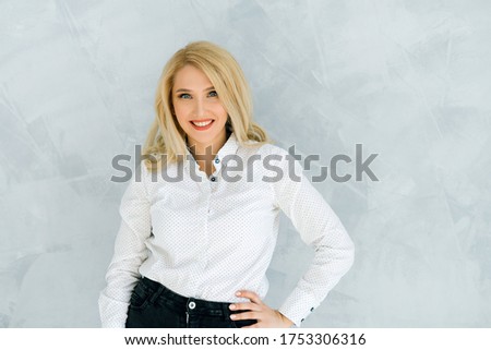 Beautiful blonde woman in the center of the frame on a light background in a white shirt posing for the camera