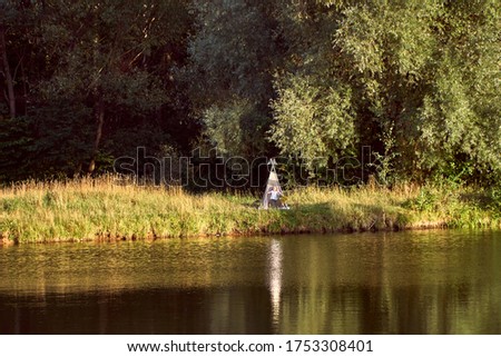 Pond on a sunny day. Wigwam on the other shore. Lake in the forest. Green fairy tale. High quality photo