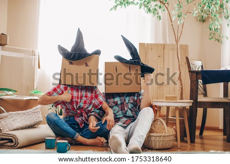 Couple With Cardboard Boxes On Their Heads Sitting On Floor After Moving House. Halloween concept.  Royalty-Free Stock Photo #1753318640