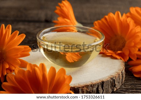 A small bowl of essential oil with fresh calendula flowers on a table