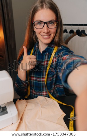 A beautiful smiling seamstress in glasses takes a selfie. The concept of a conference video with the customer.