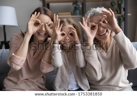 Portrait of overjoyed three generations of women have fun make funny facial gestures relax at home together, smiling small girl with young mom and mature grandmother play enjoy family weekend reunion