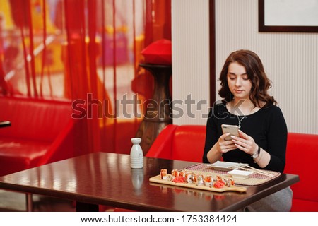 A young beautiful girl making photo by phone of sushi on traditional Japanese restaurant.