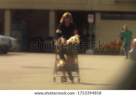 A purposefully blurry, de-focused background of a woman pushing a shopping cart through a parking lot. 