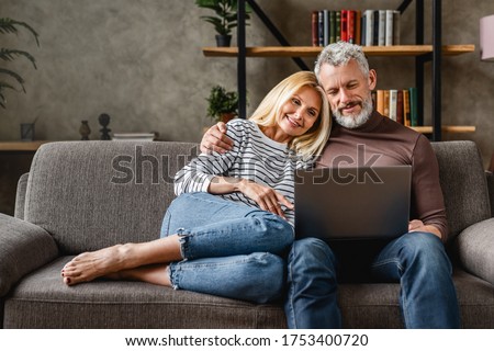 Senior couple using laptop and smiling while resting on couch at homewhile watching movie