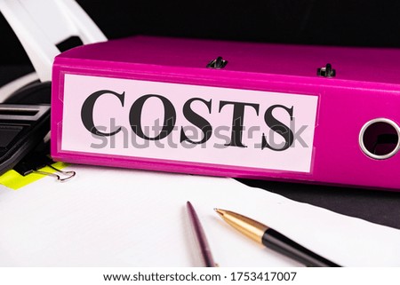 Text COSTS is written on a folder lying on a stack of papers with a pen on the table. Business concept.