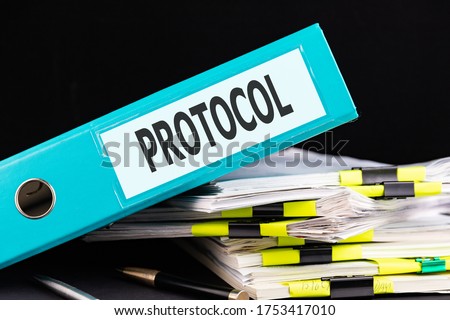 Text PROTOCOL is written on a folder lying on a stack of papers with a pen on the table. Business concept Royalty-Free Stock Photo #1753417010