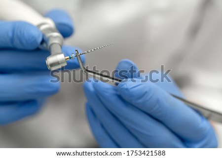 Dental tools close-up. A drill for cleaning canals in the doctor’s hand with tweezers is mounted on a mechanical drill. Royalty-Free Stock Photo #1753421588