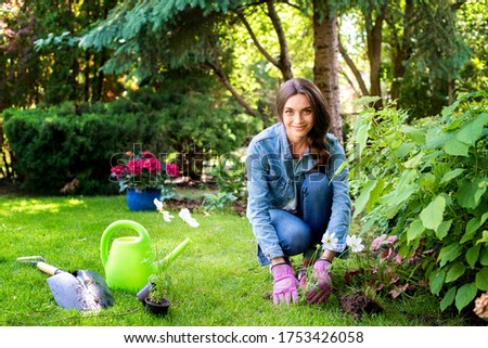 Full length shot of young woman gardening at home in the backyard. Happy woman wearing casual clothes while planting flowers.