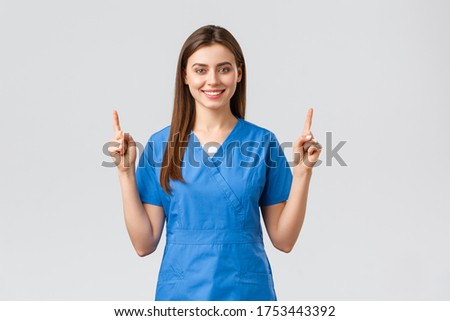Healthcare workers, prevent virus, insurance and medicine concept. Attractive nurse or doctor in blue scrubs, pointing fingers up and smiling, advertise banner, medical pills, grey background