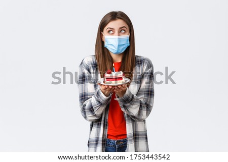 Coronavirus outbreak, lifestyle during social distancing and holidays celebration concept. Dreamy cute girl in medical mask, dreamy look up, imaging making wish as holding birthday cake with candle