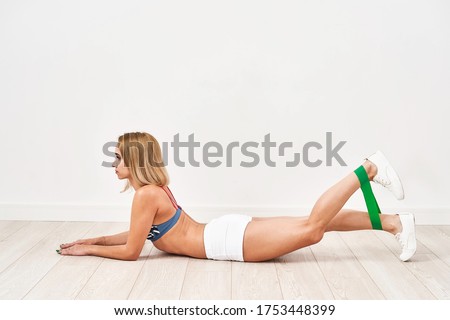 young athletic woman does exercises with a fitness elastic band. Wants to tighten the figure. A young girl in sports clothes does exercises for the leg muscles. Exercise for elastic buttocks.