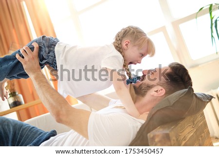 Father and daughter. Handsome young man and little cute girl play with each other, dad lies on the sofa at home and holds his daughter in his arms in the air. Laugh and smile. Father's day.