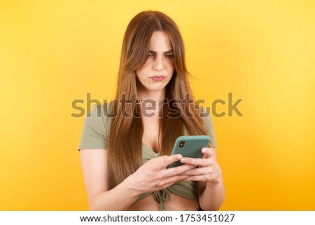Portrait of crazy impressed Young caucasian woman with long hair wearing green tshirt use cell phone reads incredible news on social media information stare, screams wow omg