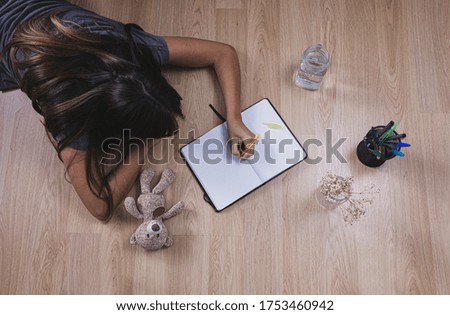 Young woman writing with in a notebook on wooden floor at home