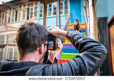 Male photographer is holding a camera and taking a photo of female girl sitting on colorful stairs. Travel photography in famous landmarks