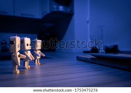 A small wooden toy robots looks at laptop in the dark. wallpaper, blured background. low light