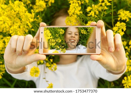 Happy smiling boy making self portrait on smartphone in meadow. young boy making selfie on smartphone laying in green grass with yellow flowers.