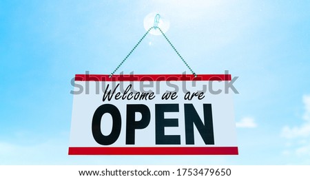 COVID-19 Open business sign saying Welcome we are OPEN hanging on window storefront reopening Retail businesses opening again. Sun blue sky summer background. end of confinement.