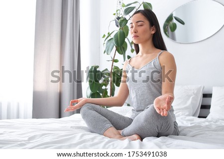 Tranquil pretty female is sitting in bedroom and relaxing during meditation in lotus position