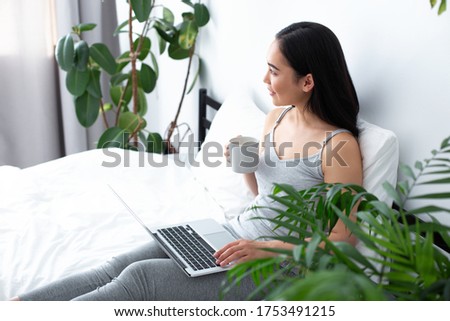 Top view of merry pretty female relaxing with mug of tea and notebook in bedroom in morning