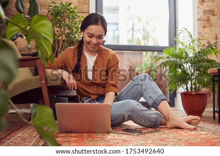 Barefoot young woman in casual clothing sitting in a comfortable pose on a floor at home using laptop
