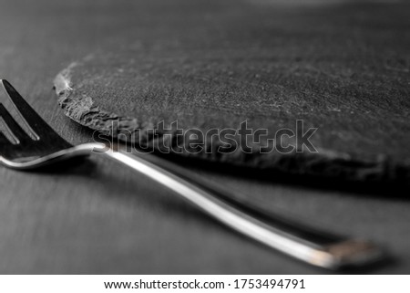 metal fork and round empty black plate from slate stone close-up. dark textured cement background