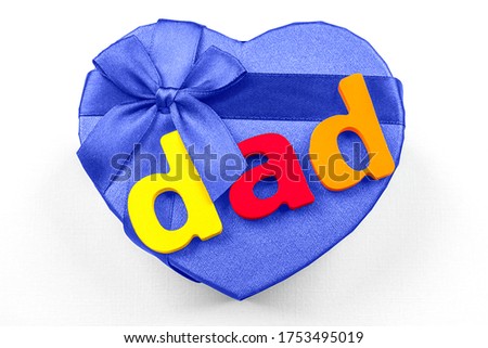 Happy Father's day. Blue gift box in the shape of a heart with a ribbon and a bow and the inscription "Dad" on a light background. Top view.