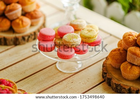 Closeup shot of colorful candy bar with french sweets macarons lying on glass plate. Macarons a placed in a middle of a frame with tasty cupcakes accompanied on both sides of horizontal picture