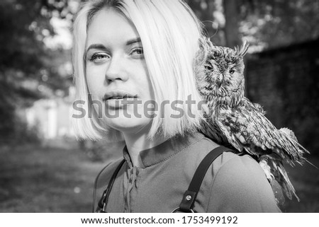 In the forest, on a bright sunny day, an owl sits on the girl’s shoulder. Black and white photo.
