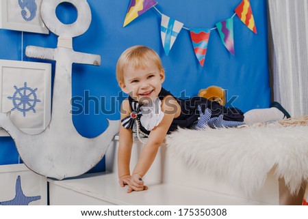 Small girl in blue dress laughing and lying on white pelt in photo studio with marine style decoration  