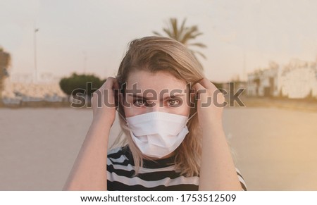 New normal. Young woman portrait putting on a mask and looking at camera. Blonde girl with a black and white stripes t-shirt. She is in a field enjoying outdoors after covid-19 quarantine Royalty-Free Stock Photo #1753512509