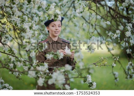 A young female pilot in uniform of Soviet Army pilots during the World War II. Military shirt and a beret. In spring blooming apple orchard. Photo in retro style.