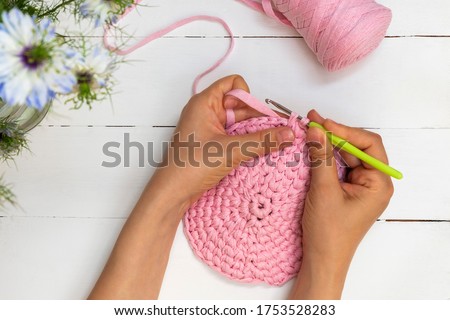 Directly above view of woman hands holding crochet hook and crocheting with ribbon yarn on white wooden table Royalty-Free Stock Photo #1753528283
