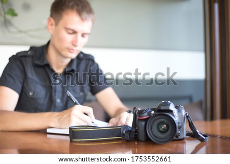 Digital camera lies on table on the background of photographer writing orders in notebook