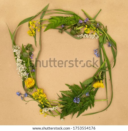 Yellow dandelion and other may flowers and herbs ring wreath ornament on rustic brown natural paper background with free copy space for text. Design template for card, invitations, wedding decor.