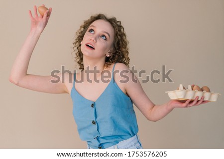 Studio shot of a cute curly woman holding an eggs - copy space on grey background. Emotional portrait