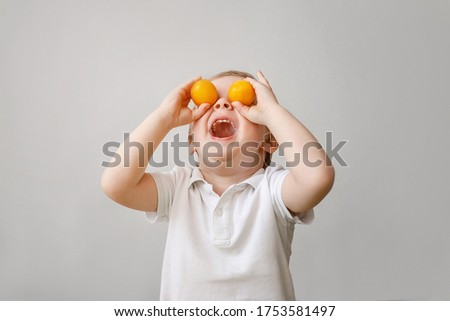 A very funny todler boy indulges with orange fruit, he put the fruit on his eyes and laughs.  Royalty-Free Stock Photo #1753581497