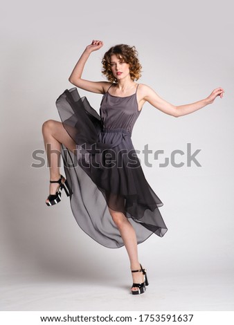 High fashion photo of a beautiful elegant young woman in a pretty dark gray dress, top, skirt, hairstyle on white, soft gray background. Studio Shot. 